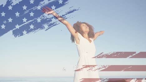 animation of american flag over african american woman raising hands at beach