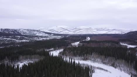 wide aerial alaska landscape with frozen winding river, snow capped hills in the background wintertime