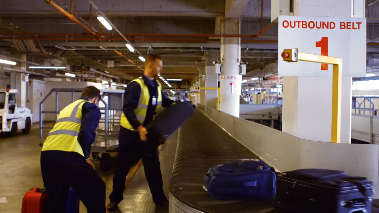 Two airport workers putting baggage on baggage carousel