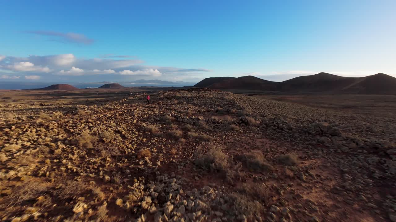 hombre de pie en terreno rocoso bajo un cielo azul claro, cerca de los volcanes en fuerteventura