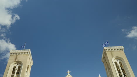 Twin-bell-towers-against-a-vibrant-blue-sky-with-Greek-flags