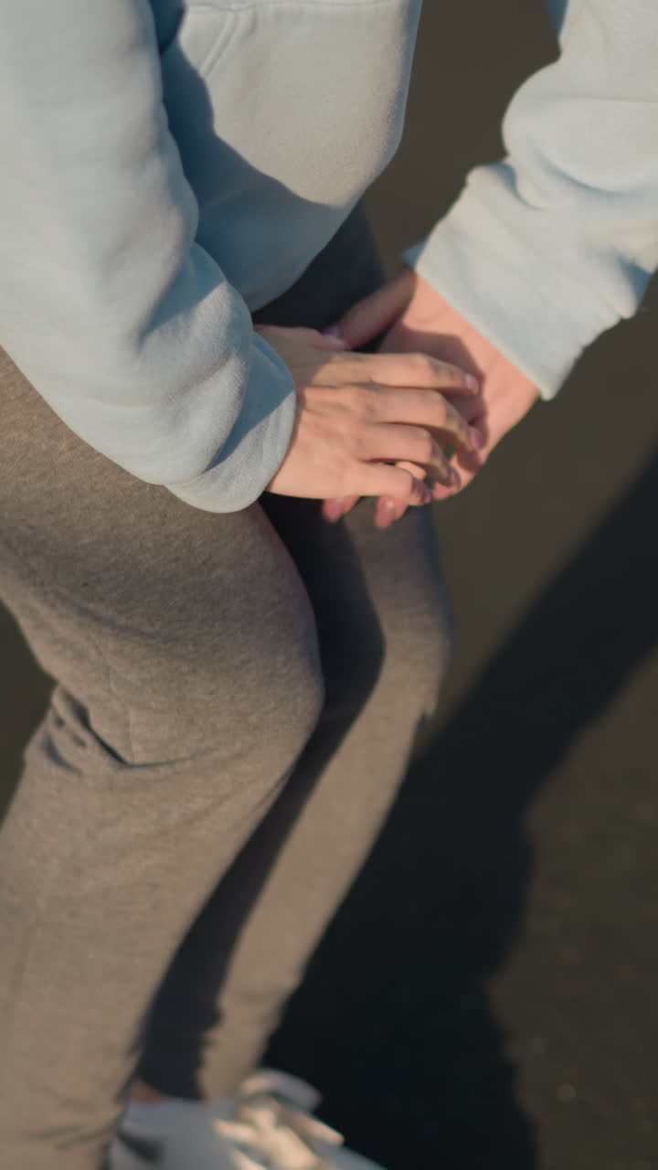 vista parcial de la dama en suéter azul haciendo ejercicio al aire libre, realizando un estiramiento arrodillado con la sombra proyectada en el suelo alquitrán bajo la luz del sol brillante