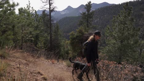 un joven excursionista de sexo masculino camina con un lindo perro de laboratorio negro a lo largo del sendero del bosque de montaña