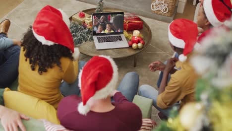 Vielfältige-Familie-Mit-Weihnachtsmützen-Und-Laptop-Für-Weihnachtsvideoanruf-Mit-Glücklicher-Familie-Auf-Dem-Bildschirm