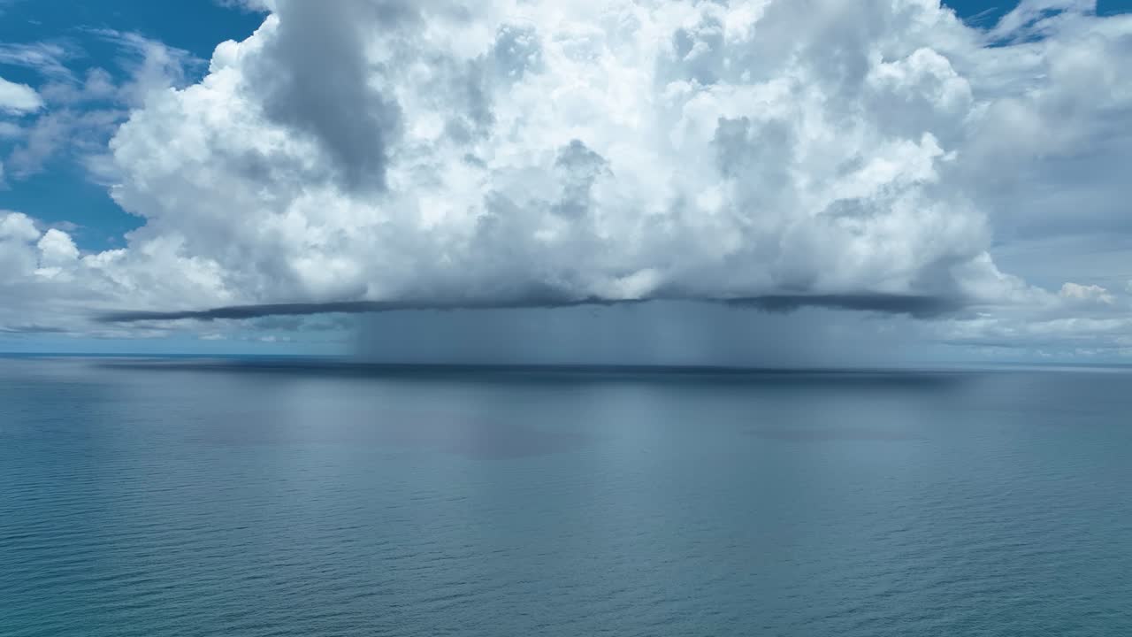 Cinematic aerial view of a tropical rainstorm forming over calm blue seas near Koh Chang, Trat, Thailand. Massive clouds and rainfall create a weather and ocean horizon scene