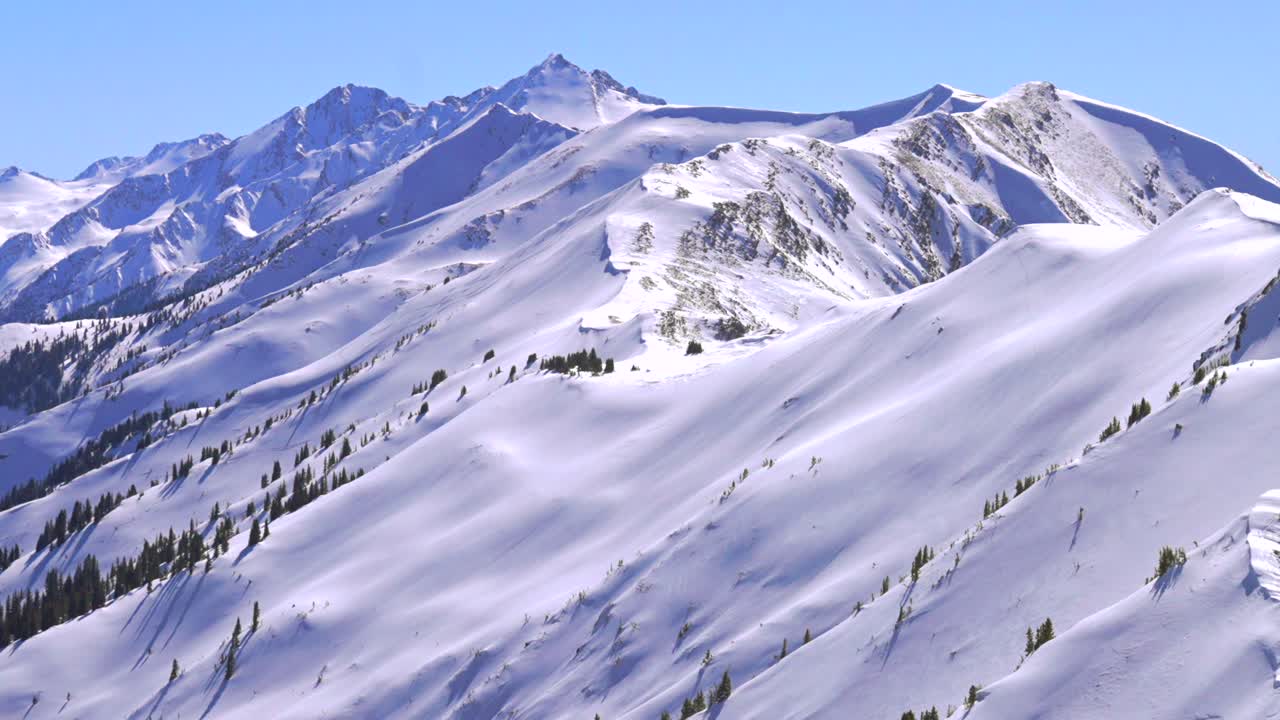 Deep powder snow winter panorama Aspen Highlands Bowl ski resort backcountry high alpine steep terrain Colorado Castle Conundrum Peak Maroon Bells Wilderness Elk Mountain range blue sky sunny zoom out