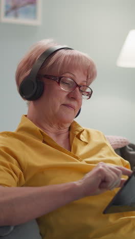 old woman in headphones with a tablet in her hands is mastering the internet, a working pensioner