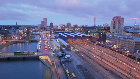 Train-arrives-at-Malmo-Centralstation-and-buses-cross-bridge,-twilight-aerial