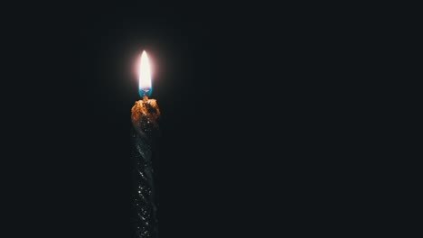 una sola vela está encendida sobre un fondo negro. llama de vela en la oscuridad