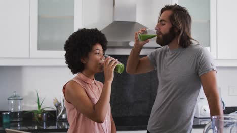 Una-Pareja-De-Raza-Mixta-Bebiendo-Batidos-De-Verduras-Juntos-En-La-Cocina-De-Casa