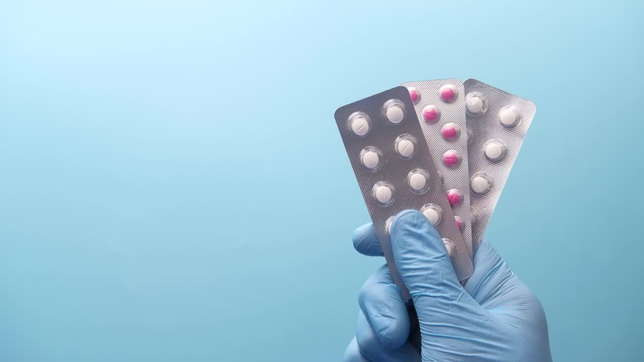 Mano enguantada sosteniendo blísteres de pastillas