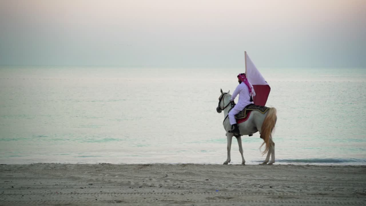 Um cavaleiro a cavalo andando e segurando a bandeira do Catar perto do mar-1
