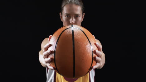 focused young caucasian woman holds a basketball in front of her on a black background