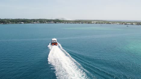 Ferry-in-The-Caribbean-sea,-arriving-to-the-island-of-Utila,-Honduras---Aerial-shot