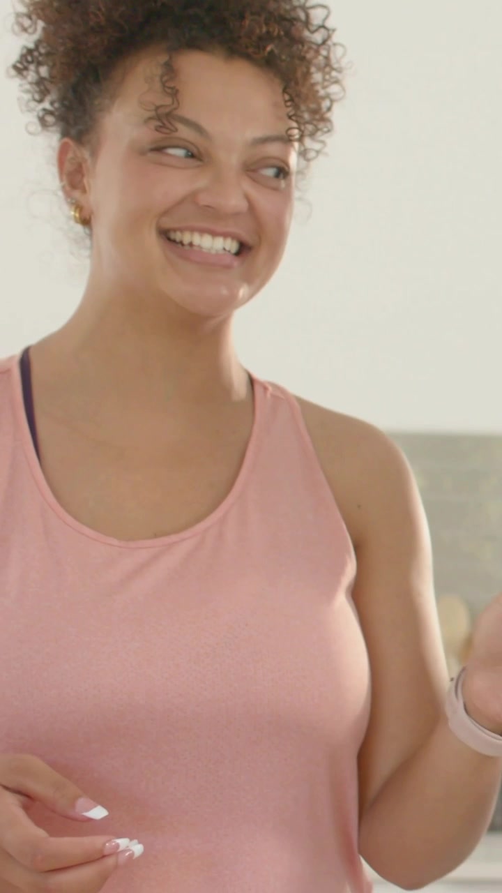 Vídeo vertical: Mulher rindo com regata rosa na cozinha enquanto uma amiga se junta, arrumando frutas em uma tábua