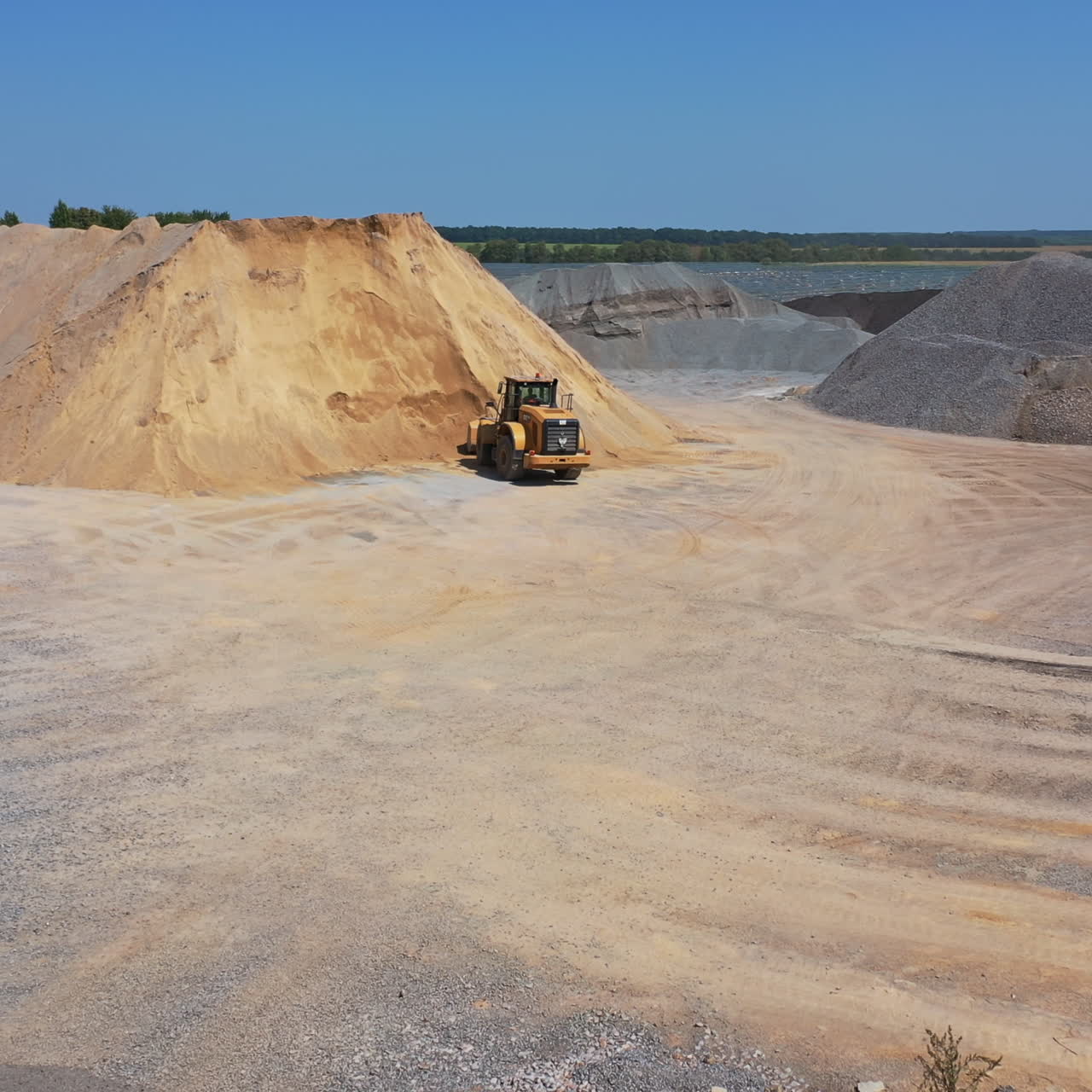 Huge piles of crushed stones and sand outdoors. Bulldozer working on the territory of asphalt plant in a sunny day. Aerial view.