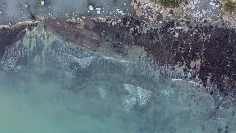 Top-down-aerial-shot-of-old-shipwreck-on-english-beach-blue-water