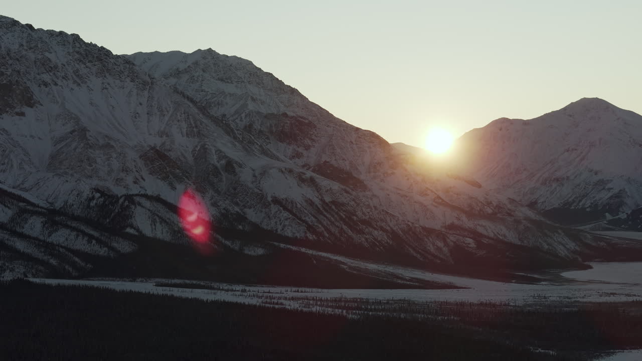 Bright Sun Between The Snowy Mountains And Forest At Sunrise Near Silver City In Yukon, Canada. - aerial shot