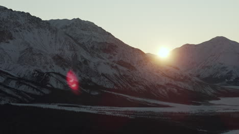 bright sun between the snowy mountains and forest at sunrise near silver city in yukon, canada. - aerial shot