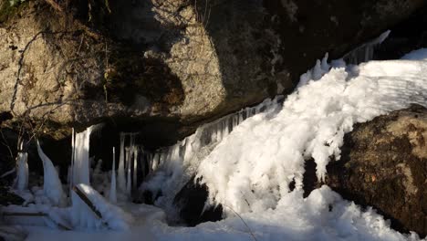 under a big rock a little waterfall springs out of a layer of ice