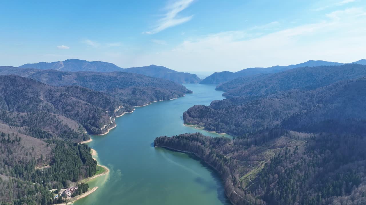 A serene river winding through lush green mountains under a clear blue sky, aerial view