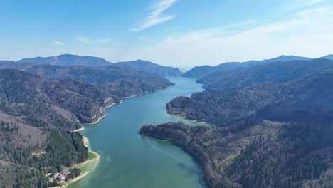 a serene river winding through lush green mountains under a clear blue sky, aerial view