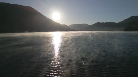 volando rápido y bajo sobre la superficie del lago brumoso hacia las montañas siluetadas al amanecer en otoño