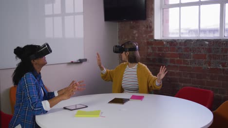 happy diverse female business colleagues sitting at table using vr headsets in meeting room