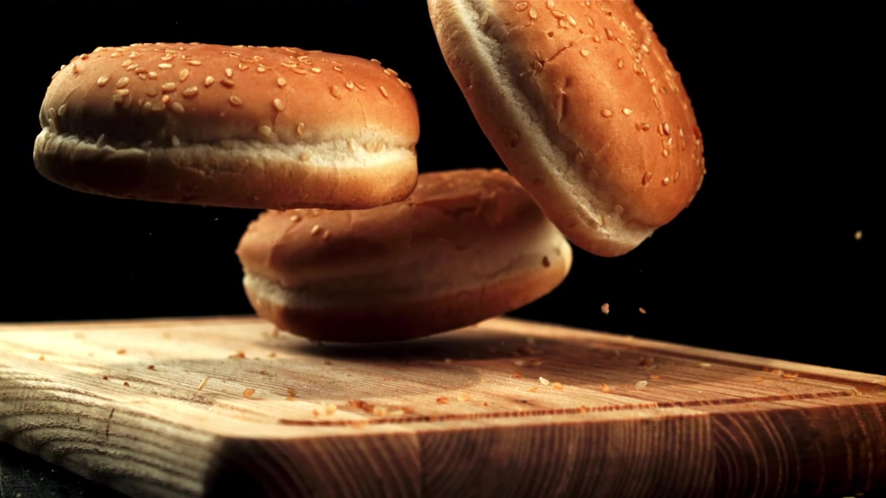Hamburger Buns Falling onto a Wooden Cutting Board in Slow Motion