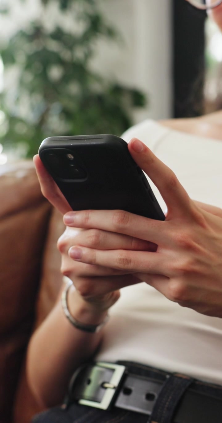 Giovane donna che usa lo smartphone seduta su un divano in pelle