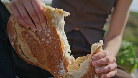 hands breaking fresh bread on outdoor picnic closeup. hungry girl baguette