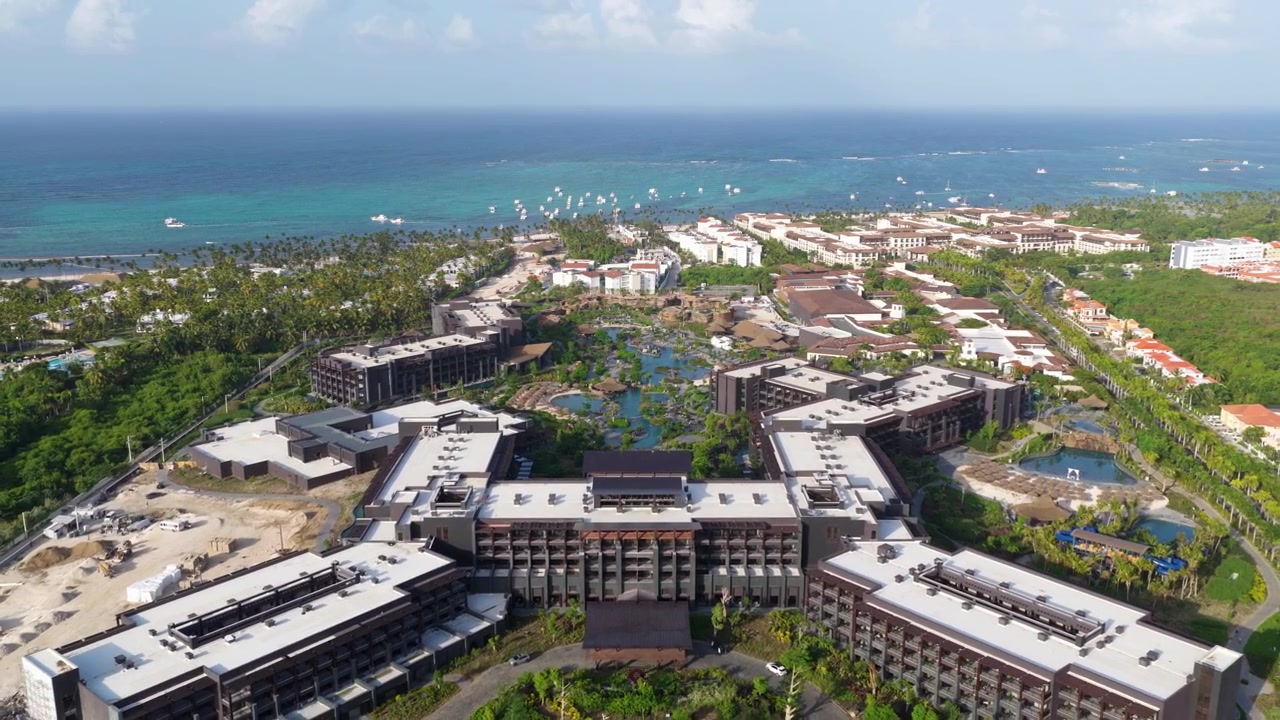 Vista drone che si allontana e si alza lentamente sopra il Lopesan Caoba Resort, rivelando piscine tropicali, edifici dell'hotel, giardini lussureggianti e il Mar dei Caraibi a Punta Cana, Repubblica Dominicana.