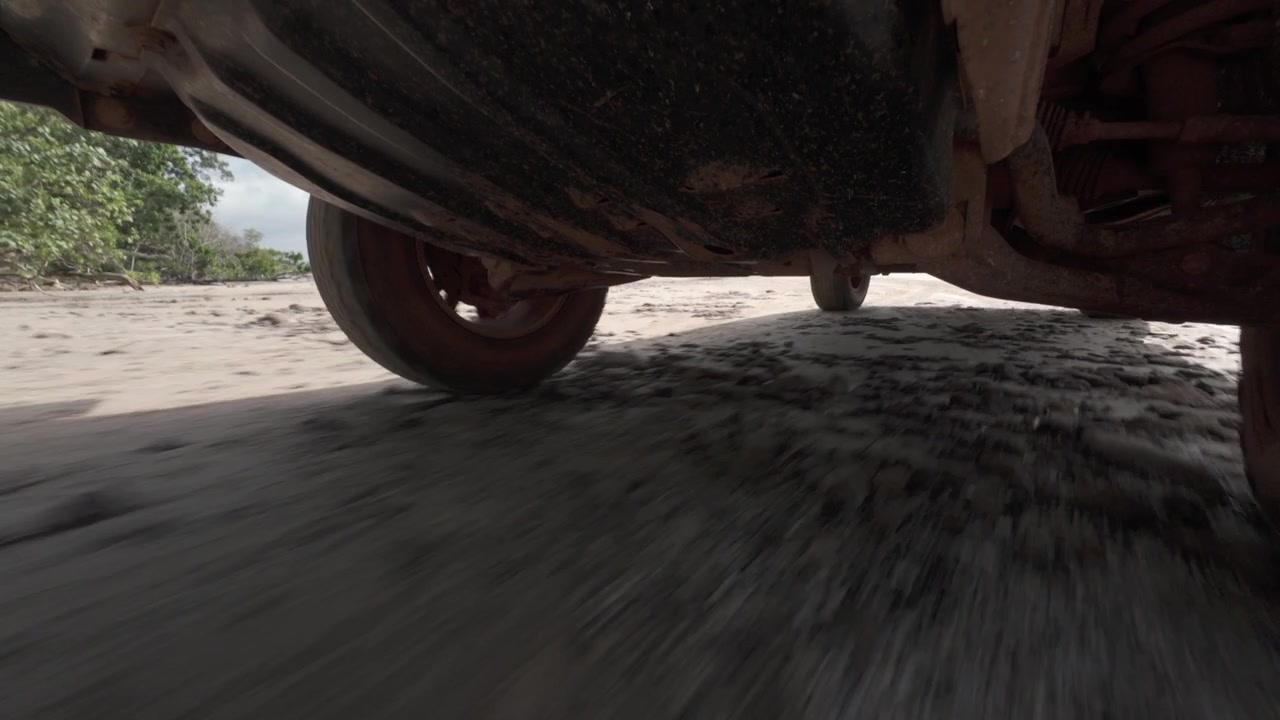 POV (punto di vista) del sottoscocca montato sotto un veicolo 4x4 che guida lungo una spiaggia remota e deserta a Cape York, Australia. Concetto di avventura fuoristrada, guida sulla spiaggia, viaggio overland. Clip 2
