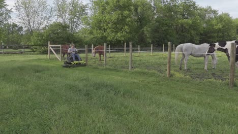 hombre recortando la hierba con una segadora eléctrica de giro cero cerca de los pastos para caballos