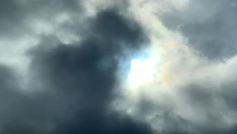 sunlight piercing through dark ominous clouds creating iridescent colors around the sun