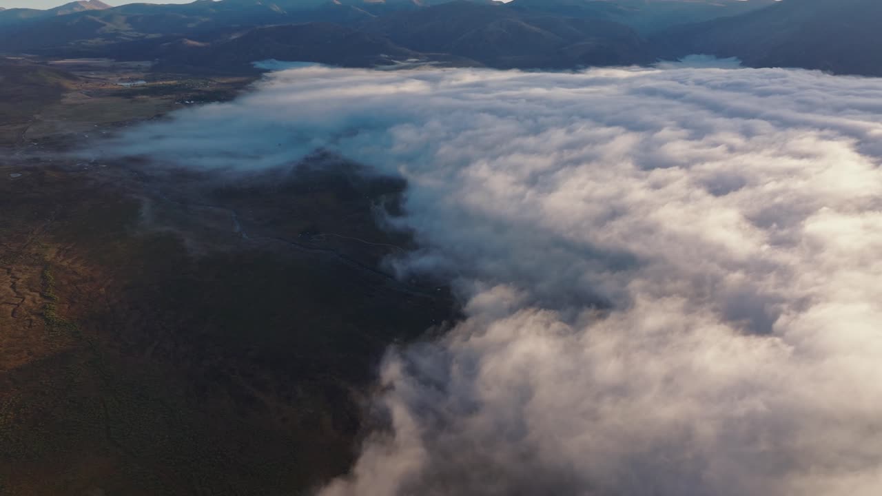 Panorâmica aérea de drone em alta altitude, com névoa cobrindo Grand Lake, Colorado, EUA, e raios de luz nas nuvens.
