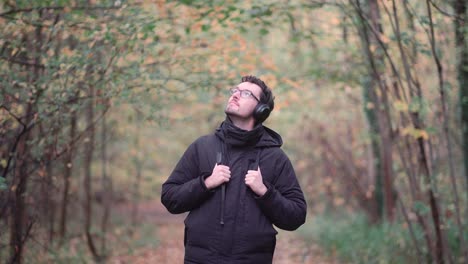 Joven-Europeo-Con-Auriculares-En-Un-Vibrante-Bosque-Mixto-De-Otoño,-Observando-Coloridas-Hojas-De-Otoño