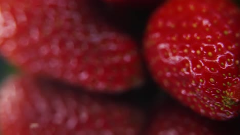 macro detailed video of a pile of strawberries, red strawberry, green leaf, tiny yellow seeds, on a rotating reflection stand, smooth movement