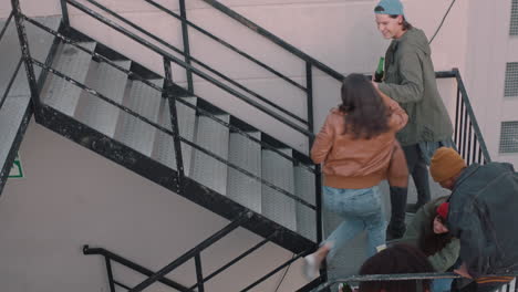 group-of-young-multiracial-friends-walking-up-fire-escape-stairs-to-rooftop-party-chatting-sharing-excitement-for-weekend-celebration