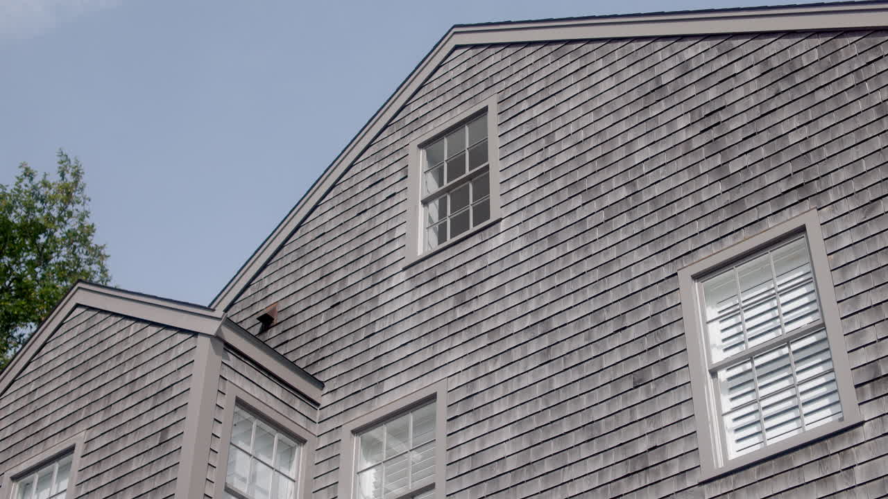 Ripresa con gimbal laterale da camion di una casa con scandole di cedro a Nantucket, Massachusetts, che mostra la classica architettura del New England sotto un cielo azzurro brillante
