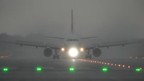 airplane approaches runway in rainy and foggy conditions, illuminated lights guide the landing, showcasing aviation in challenging weather