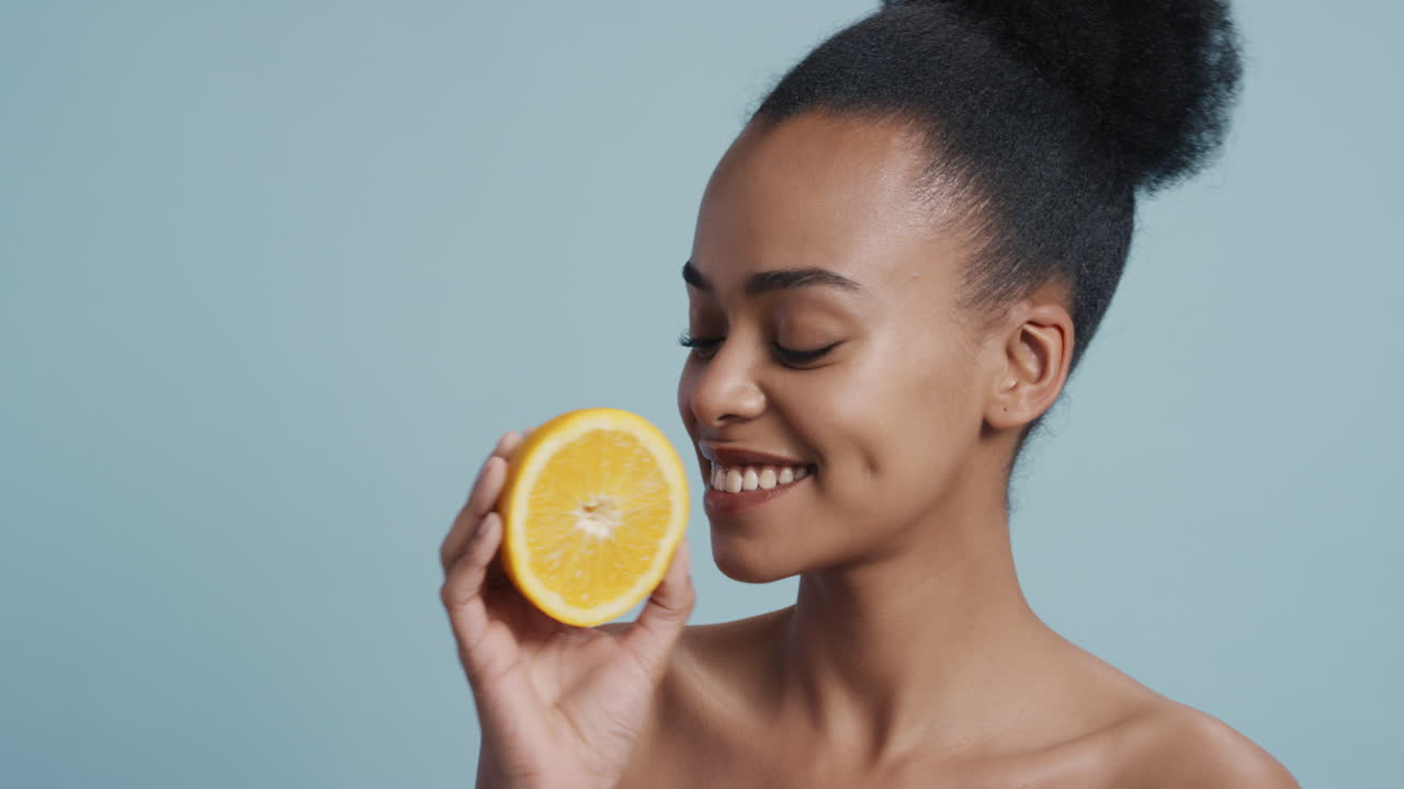 portret aantrekkelijke jonge afro-amerikaanse vrouw met citroen glimlachend genietend van natuurlijke gezonde huidverzorging essentie mooie vrouw met perfecte teint op blauwe achtergrond
