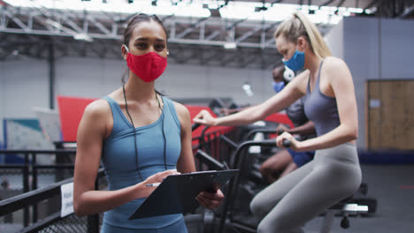 Entrenadora-De-Fitness-Femenina-De-Raza-Mixta-Con-Mascarilla-En-El-Gimnasio