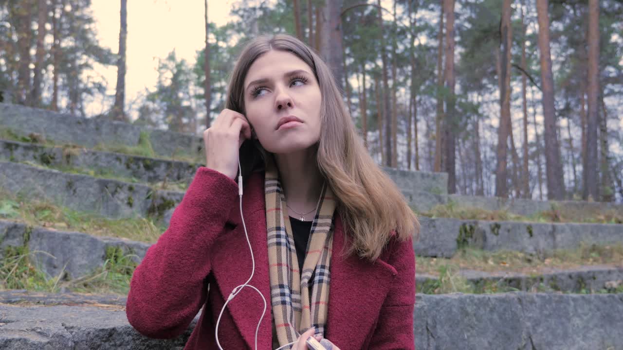 una mujer joven escuchando música en un bosque.