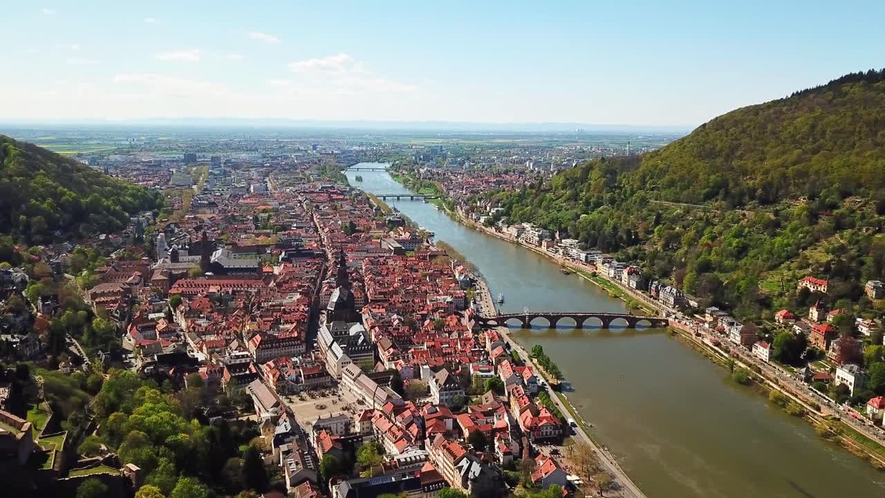 A breathtaking aerial perspective of Heidelberg, Germany, highlighting the historic Old Town, Neckar River, lush hills, and the iconic Heidelberg Castle with its red-roofed charm surroundings