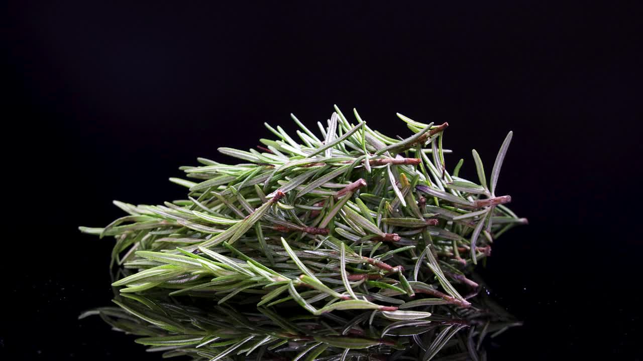 A bundle of rosemary rotates smoothly on a reflective black surface, highlighting its texture and vibrant green color