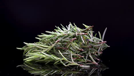 a bundle of rosemary rotates smoothly on a reflective black surface, highlighting its texture and vibrant green color