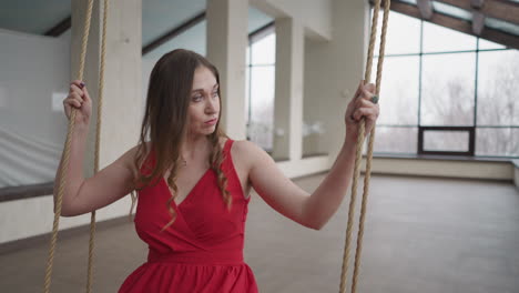 mujer modelo graciosamente se sienta en el columpio de cuerda. modelo disfruta del movimiento de balanceo mirando a la ventana que irradia aura de sofisticación en la residencia. aura de gracia