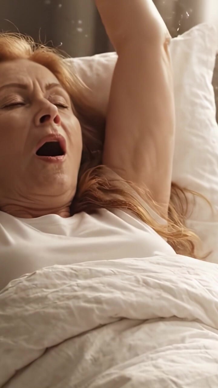A Serene Moment of Tranquility: An Older Woman with Long Hair Feels Peaceful While Resting Comfortably in Bed, Surrounded by Soft Bedding and Gentle Light