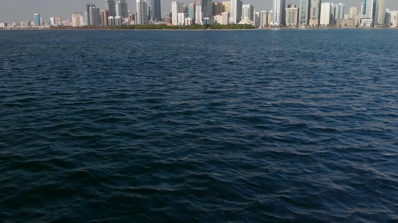 Aerial Drone flies over Sharjah's Khalid lake towards futuristic Al Majaz district on a beautiful day, Residential Modern skyscraper buildings in the United Arab Emirates